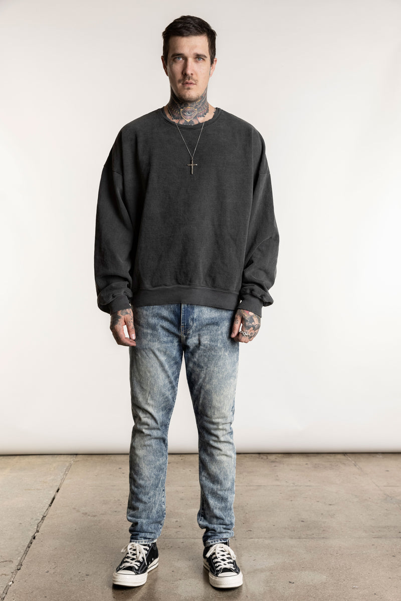 A male model wearing a gray oversized dropped shoulder sweatshirt with ribbed neckband, cuffs, and hem, paired with blue jeans.